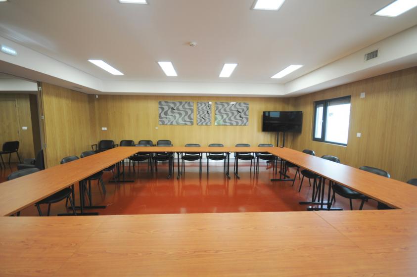 Sala de reuniões com mesas, cadeiras e uma televisão